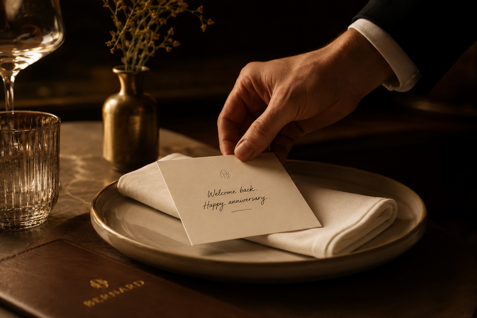 A server places a personalised anniversary card on an ivory napkin in a warm, cinematic fine-dining setting.